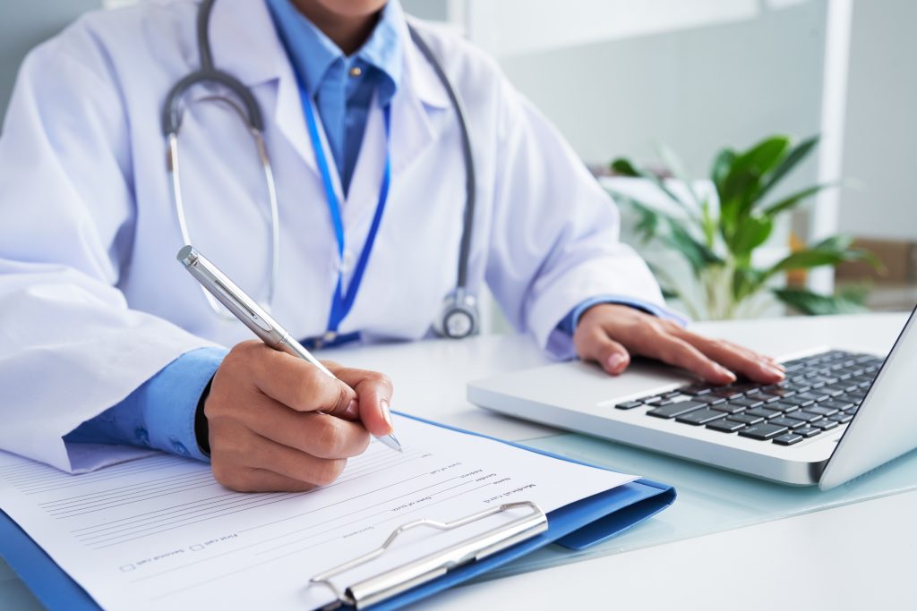 Médico comprobando información en programa informático antes de llenar la tarjeta médica