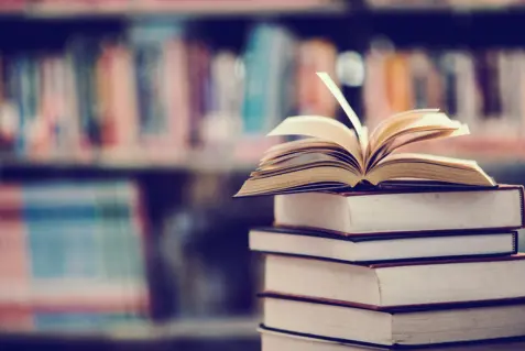 Una pila de libros sobre una mesa frente a una biblioteca.