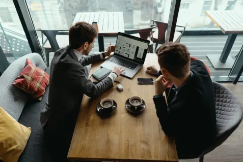 Dos hombres sentados en una mesa con computadoras portátiles.