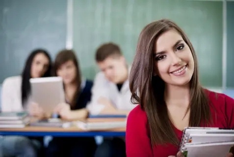 grupo de estudiantes y frente a ellos una Joven mujer sonriente sosteniendo una carpeta.