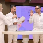 Posesión del rector en la Universidad Popular del Cesar con un hombre juramentando con la mano levantada frente a el presidente del consejo superior y una asistente, todos vestidos de blanco.
