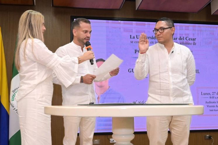 Posesión del rector en la Universidad Popular del Cesar con un hombre juramentando con la mano levantada frente a el presidente del consejo superior y una asistente, todos vestidos de blanco.